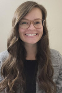 Board Certified Behavior Analyst woman with brown hair wearing glasses beams brightly, radiating warmth and confidence.